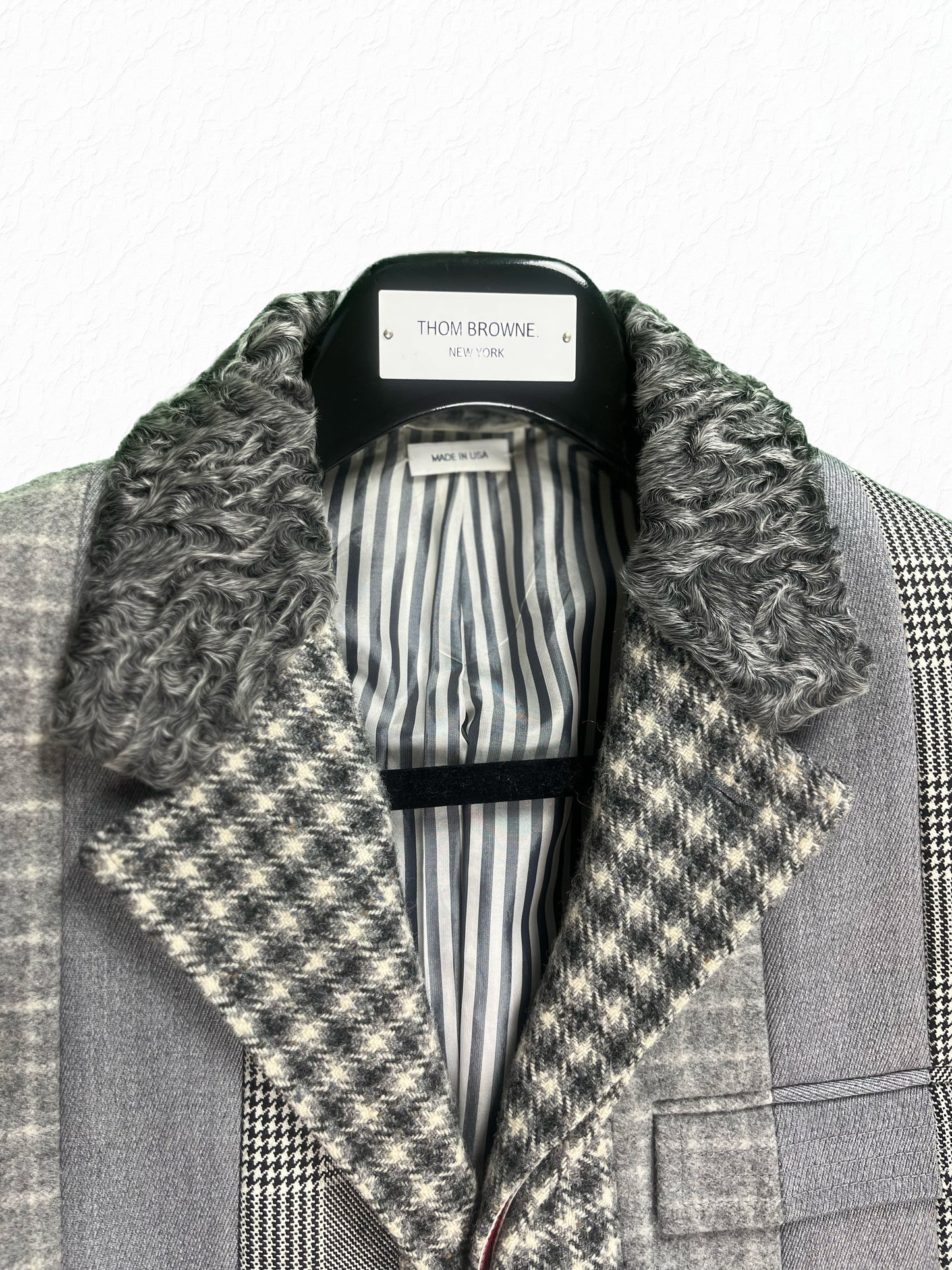 Grey striped lining and astrakhan collar on Thom Browne paneled overcoat